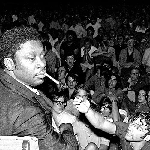 B.B. King with a cigarette in his mouth facing a large, seated concert audience.