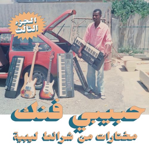 A man standing by a red car holding a keyboard surrounded by musical instruments.