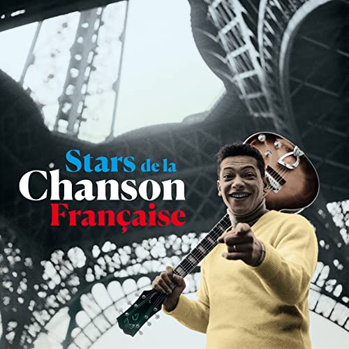 A man in a yellow sweater holding a guitar in front of the Eiffel Tower.