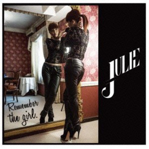 A woman in a black lace top and leather pants stands before a mirror.