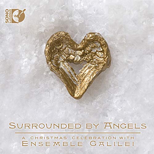 A gold heart-shaped ornament made of angel wings rests on a bed of snow.