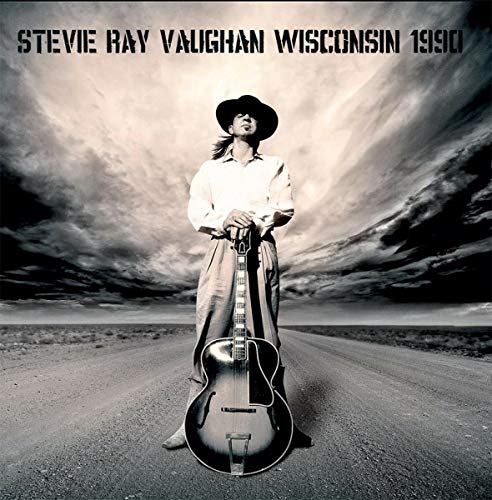 Stevie Ray Vaughan with guitar on a road under stormy skies.