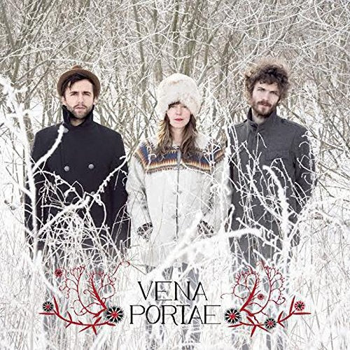 Three people in winter clothing stand before a snowy, bare tree background.