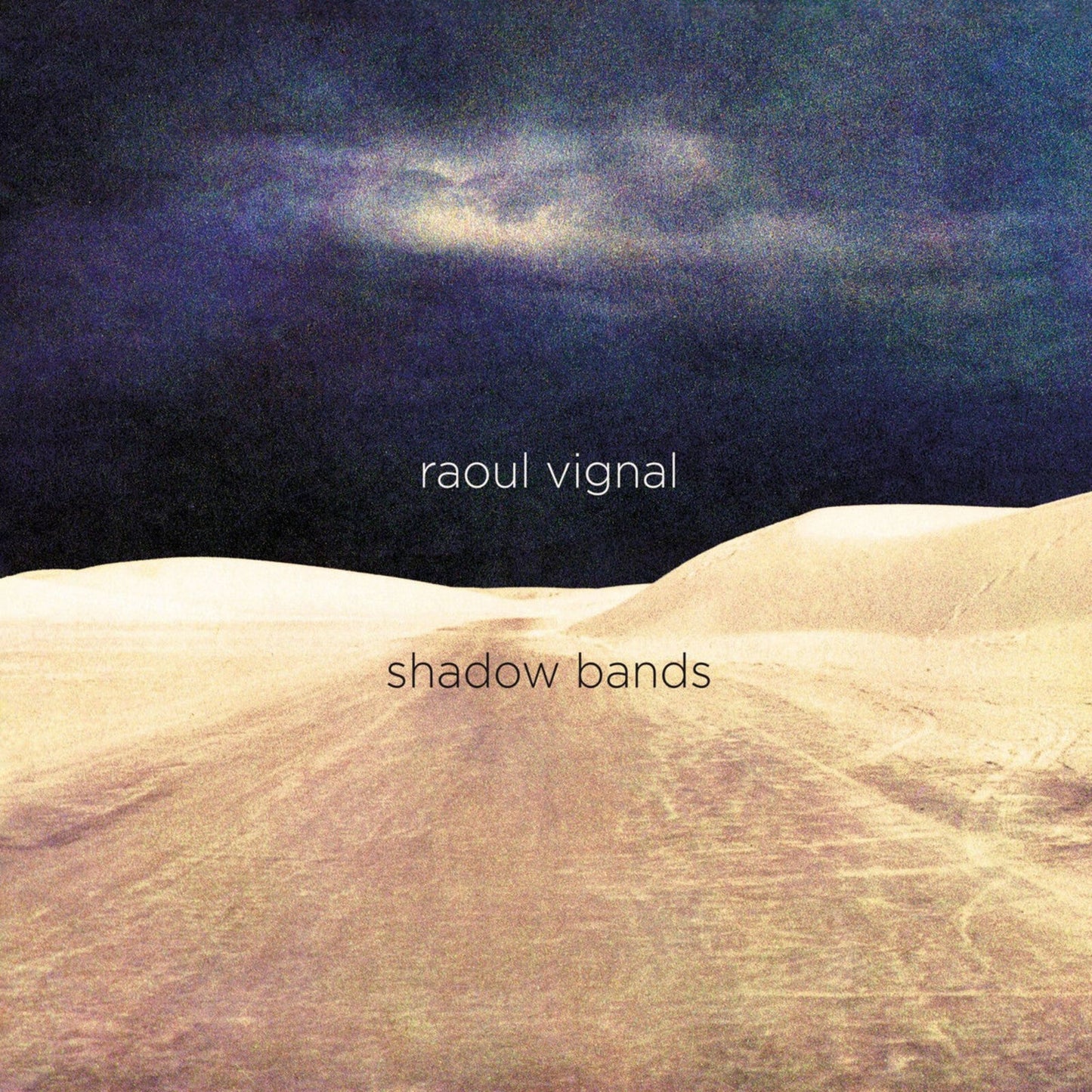 Album cover: sandy landscape under a dark, cloudy sky with text.
