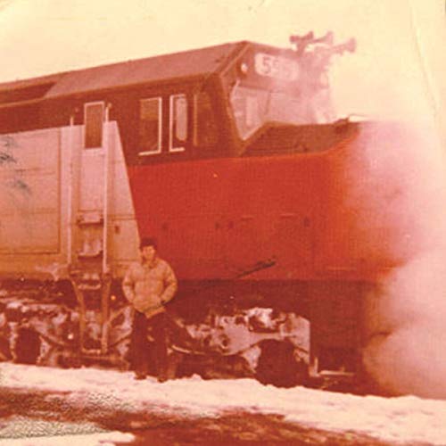 A man in a tan jacket stands beside a red train engine in the snow.