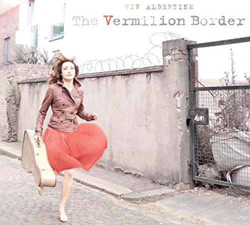 Woman running with guitar case near a wall with barbed wire.