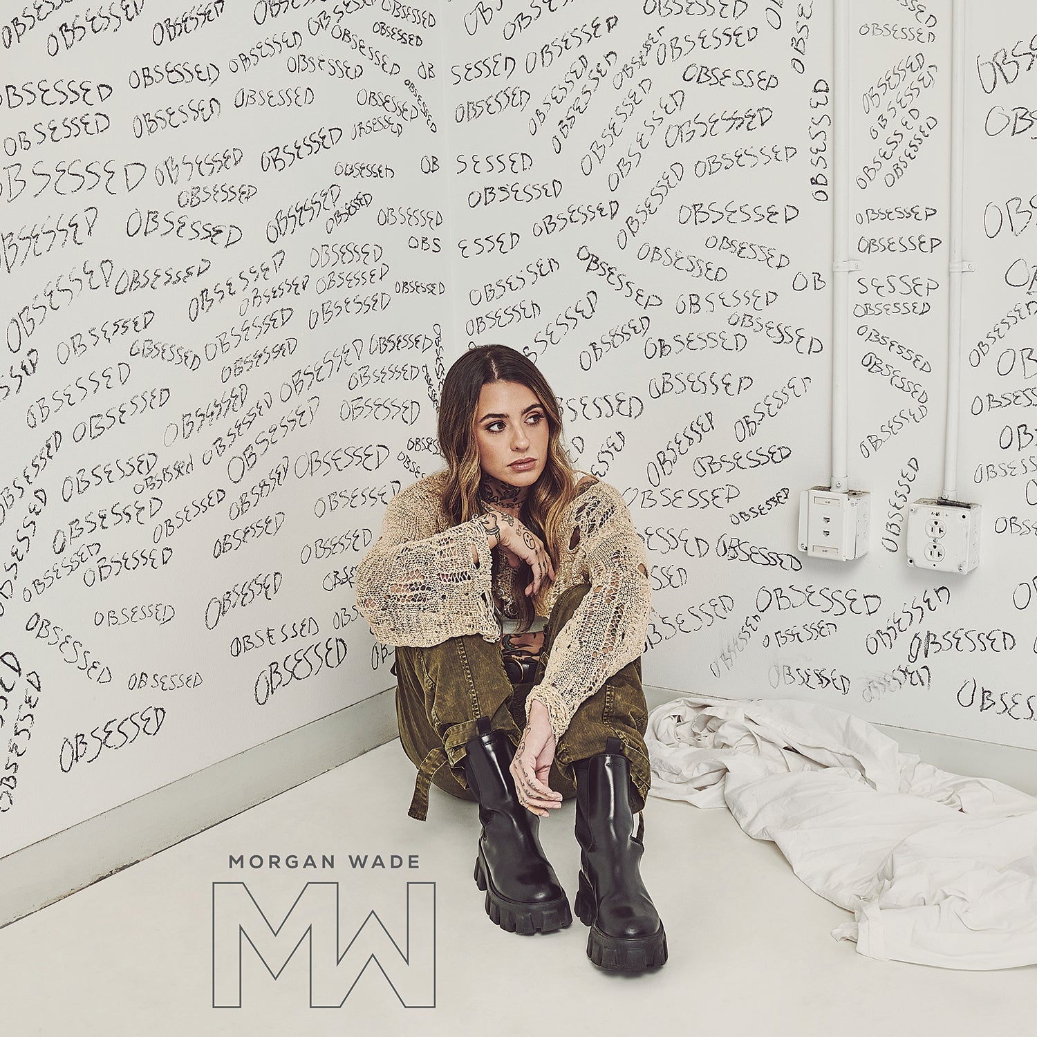 Morgan Wade sits in a corner with walls covered in the handwritten word Obsessed.