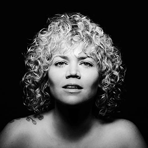 Black and white portrait of a woman with curly hair against a black background.