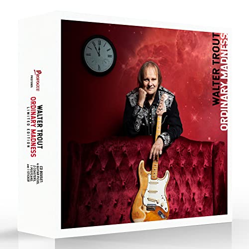 Walter Trout posing with an electric guitar against a red background with a clock.