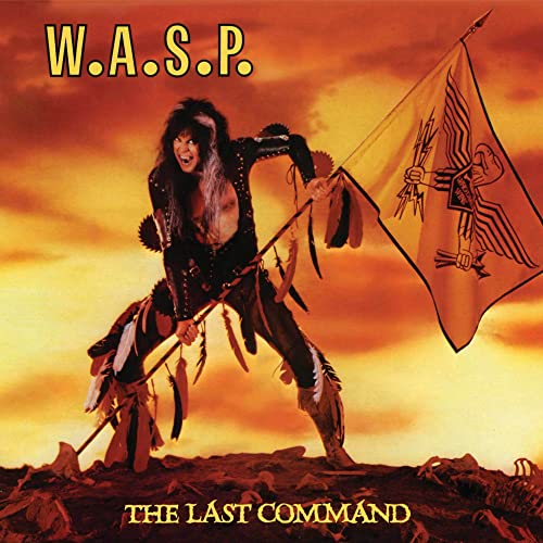 W.A.S.P. band member holding a flag against a sunset background on a rocky landscape.