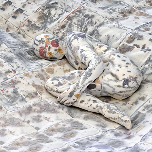Person covered in patterned fabric lying on a textured, tiled surface.