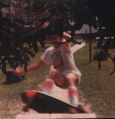 Blurry photo of a person in a white t-shirt riding a skateboard outdoors.