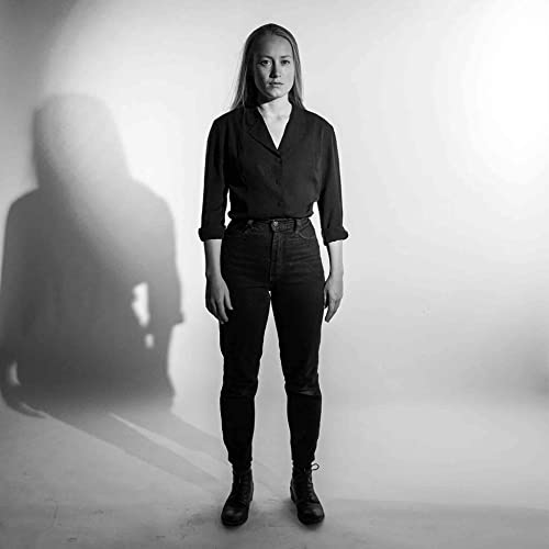 A person in a black shirt and jeans stands against a white background.
