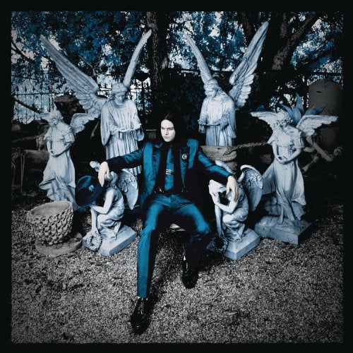 Jack White in suit seated among stone angel statues in a graveyard.