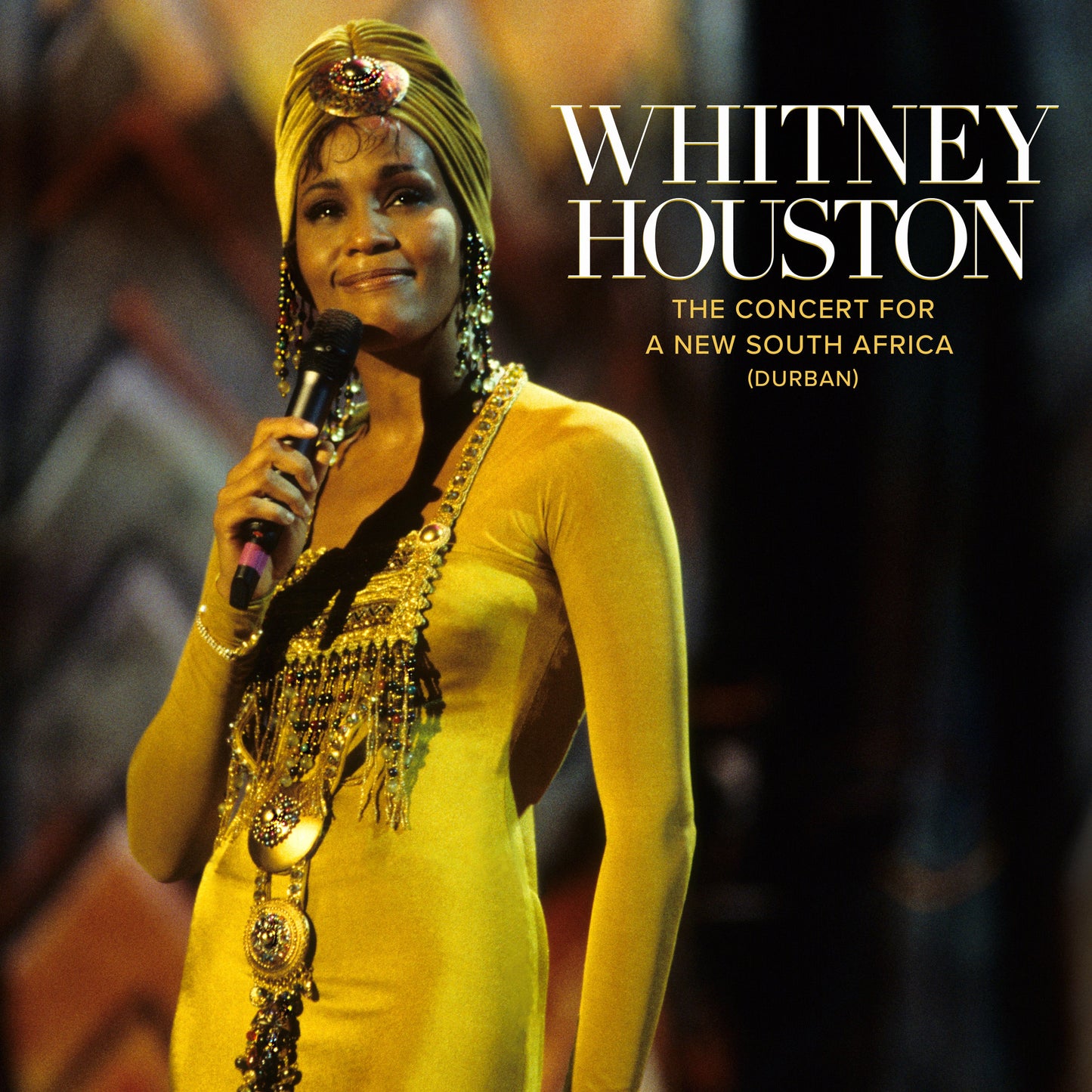 Whitney Houston in yellow gown singing into a microphone onstage.