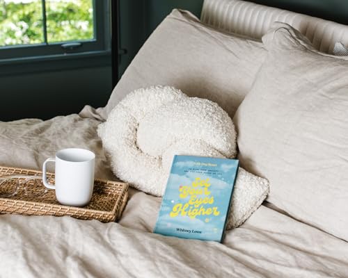 Devotional book “Set Your Eyes Higher” on a bed with a mug.