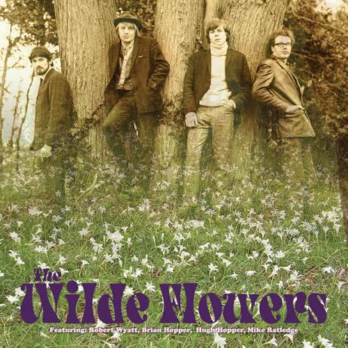 Four men in jackets standing in a field of white flowers by a tree.