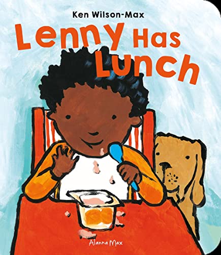A young boy with a spoon sits at a table with a dog nearby.