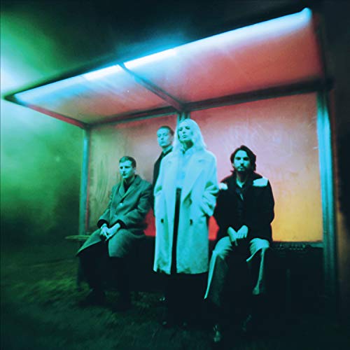 Wolf Alice band members seated under a brightly lit bus shelter.