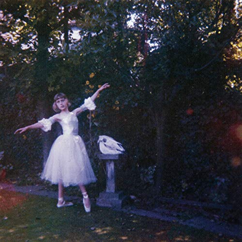 A ballerina in a white dress stands in a garden beside a bird skull.