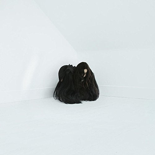 Person with long dark hair curled in a white corner.