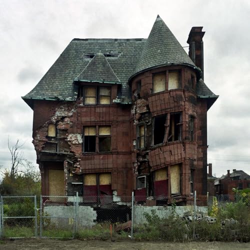 Dilapidated red brick house with missing sections, boarded windows, and a gray sky.