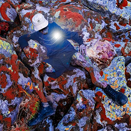 Person in blue clothing reclines among colorful, lichen-covered rocks.