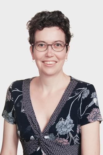 A woman with short curly hair and glasses wearing a floral print dress.