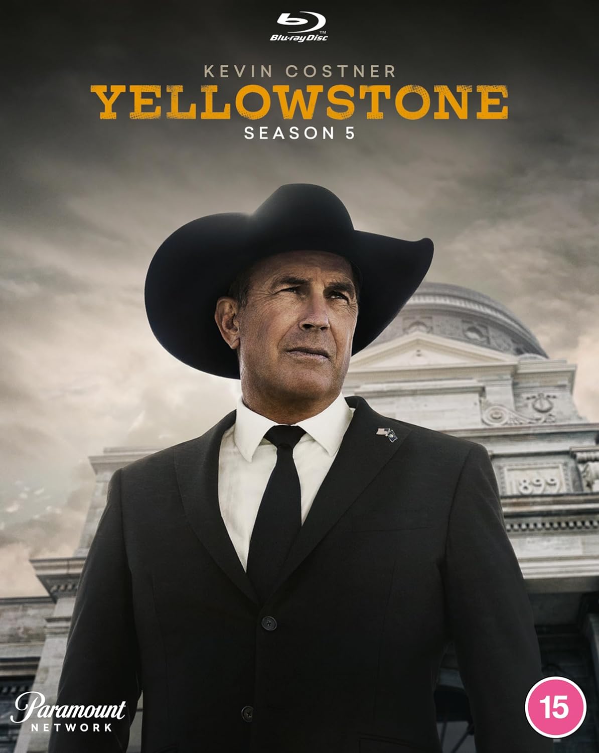 Kevin Costner wearing a cowboy hat and suit in front of a building.