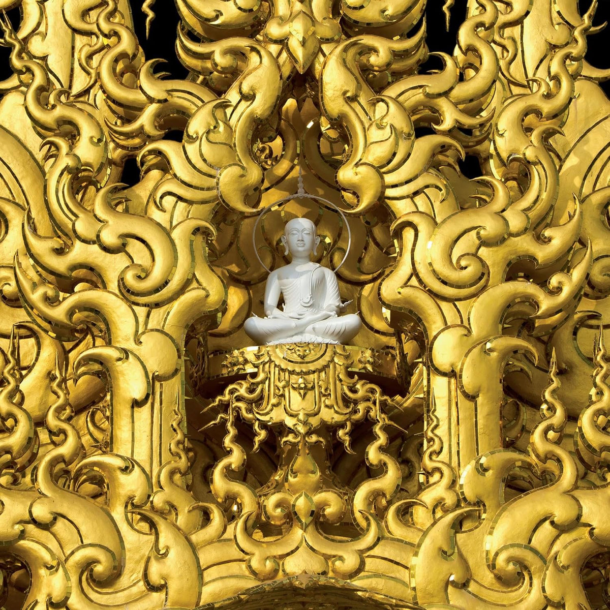 Golden ornate carving frames a white Buddha in a meditative pose.