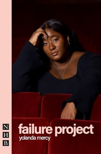 A woman in a black shirt sits in a red theater seat, looking forward.