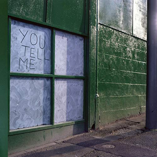 "Green building exterior with a window displaying 'You Tell Me' on frosted glass."