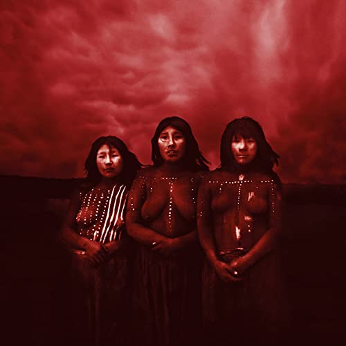 Three Indigenous women with body paint against a red, cloudy sky.
