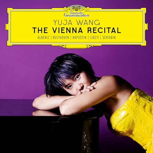 Yuja Wang in a yellow dress leaning on a piano against a purple background.