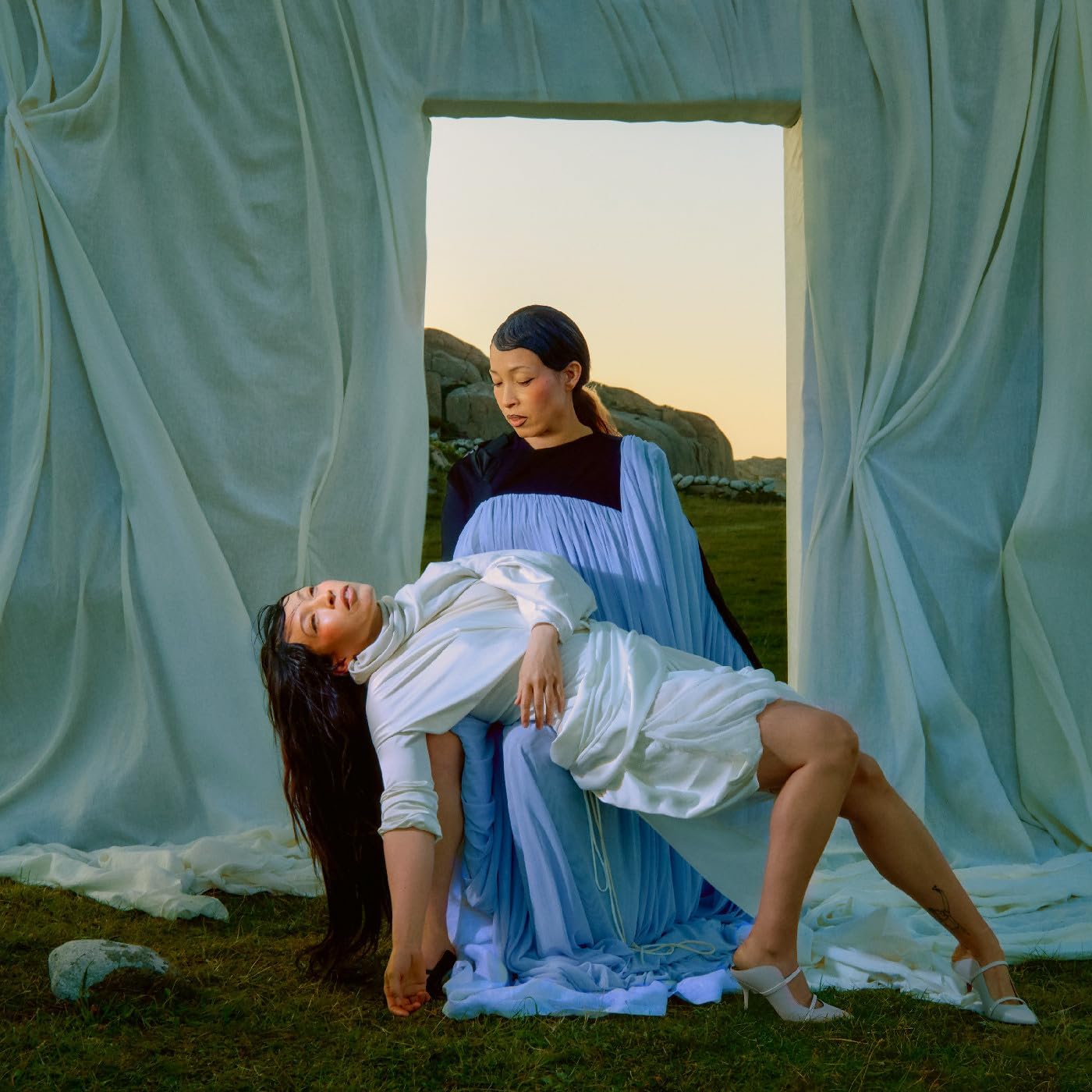 A woman in a blue dress holds another woman in a white dress outdoors.