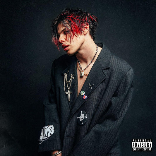 Yungblud with red-streaked hair wearing a dark blazer with pins and chains.
