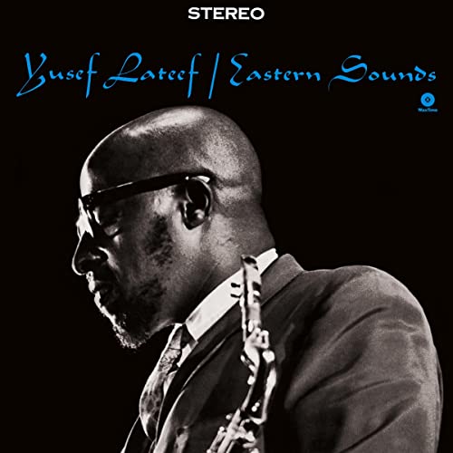 Black and white portrait of Yusef Lateef playing saxophone against a dark background.