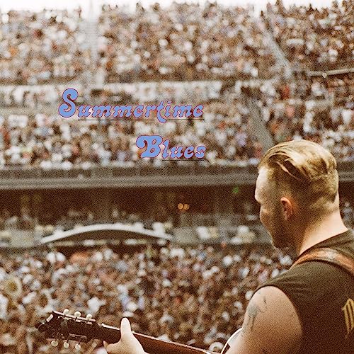Zach Bryan playing guitar before a large, blurred stadium crowd.