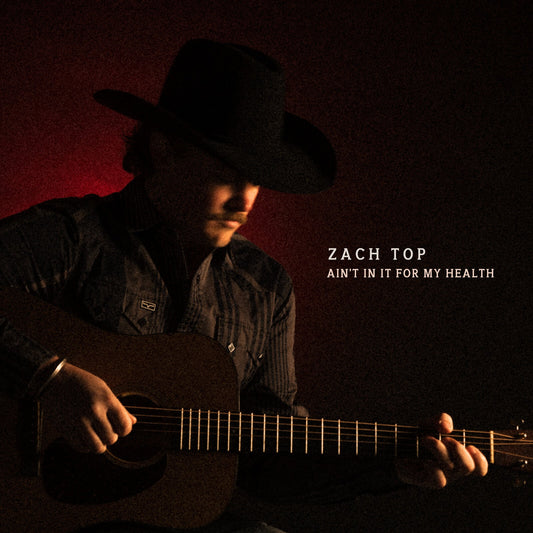 A man in a cowboy hat plays an acoustic guitar against a dark red background.