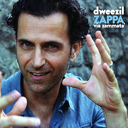 Dweezil Zappa smiling with hands raised against a stone background on album cover.