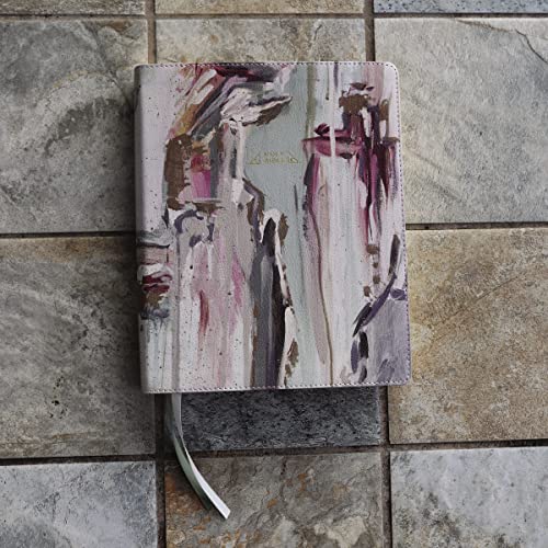 A Bible with a cream and multi-color abstract painted cover resting on stone tiles.