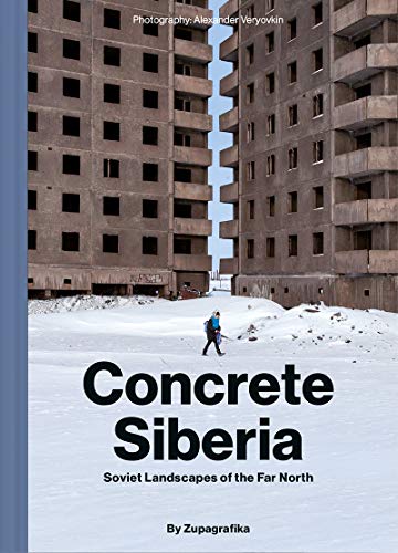 A person walks through snow between two tall, brutalist concrete Soviet apartment buildings.