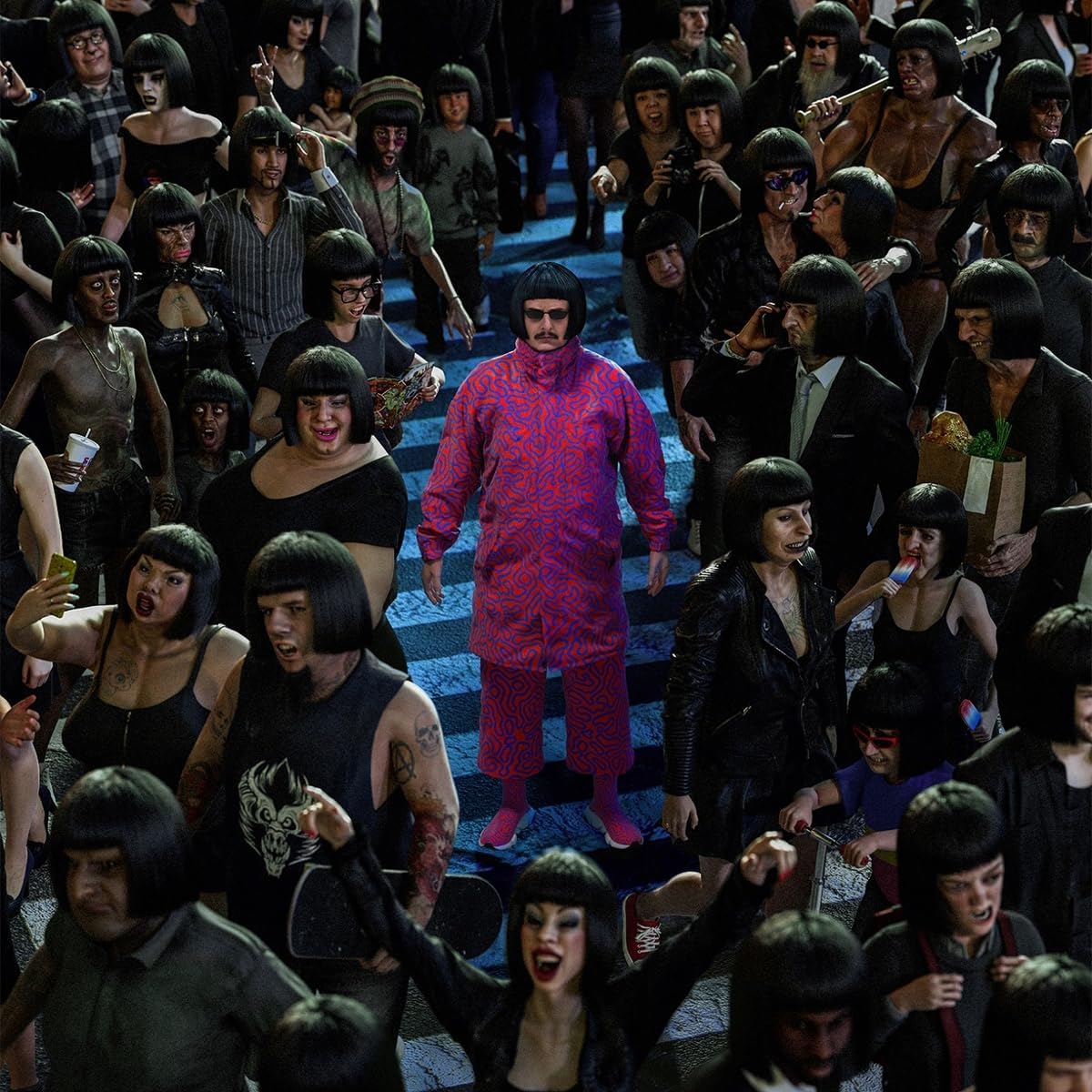 "Man in red stands on stairs surrounded by crowd with identical black bowl haircuts."