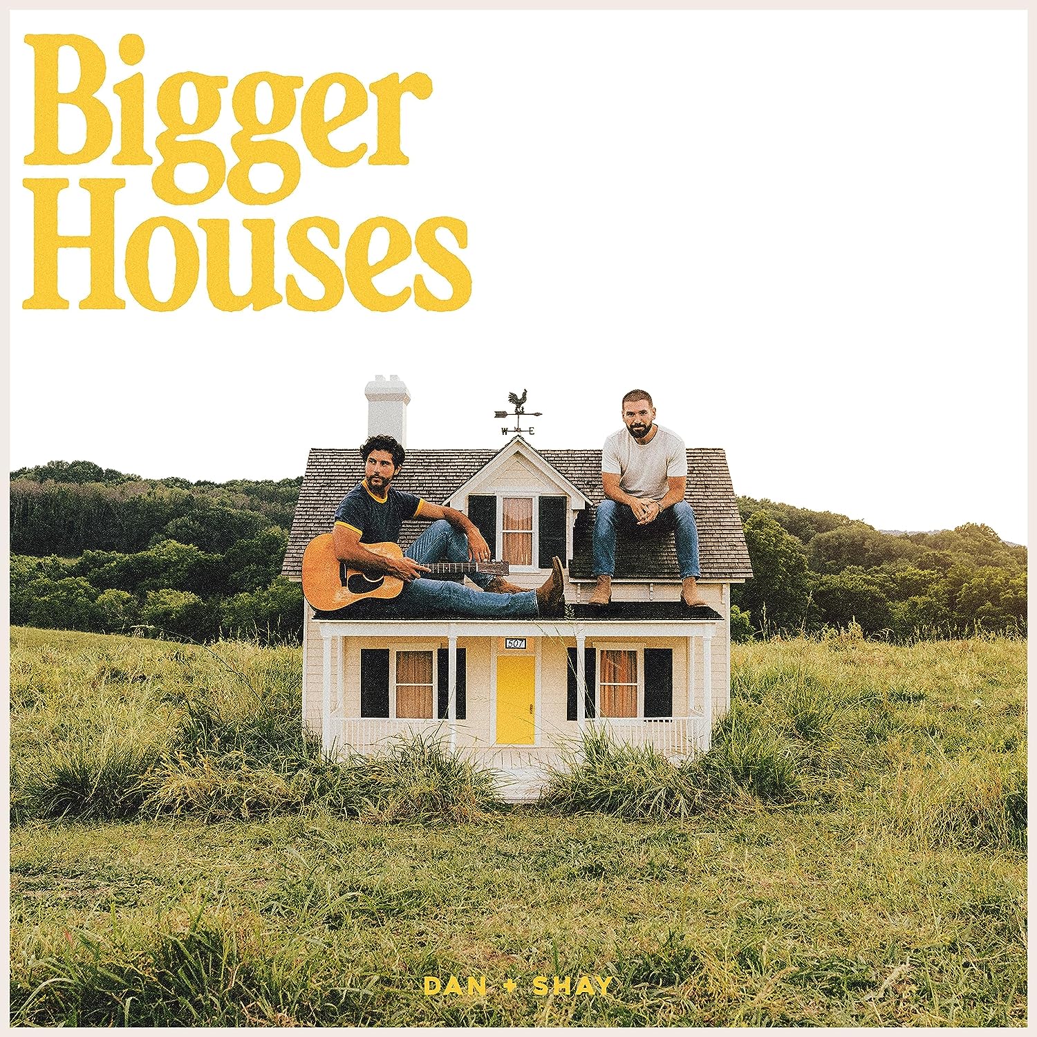 "Album cover with two men sitting on a small house in a field."