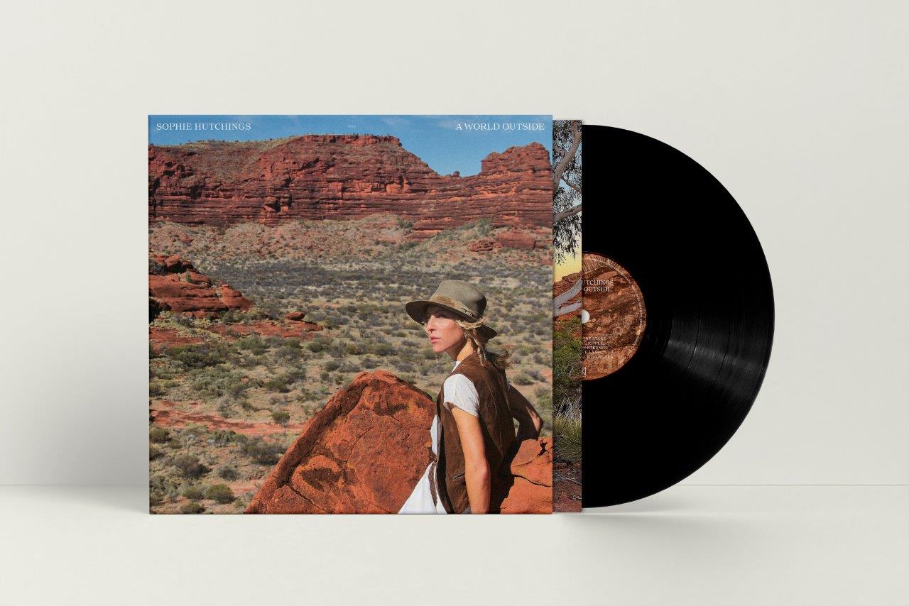 The image shows a vinyl record titled "A World Outside" by Sophie Hutchings. Alt text: Vinyl record cover with desert landscape and woman wearing a hat.