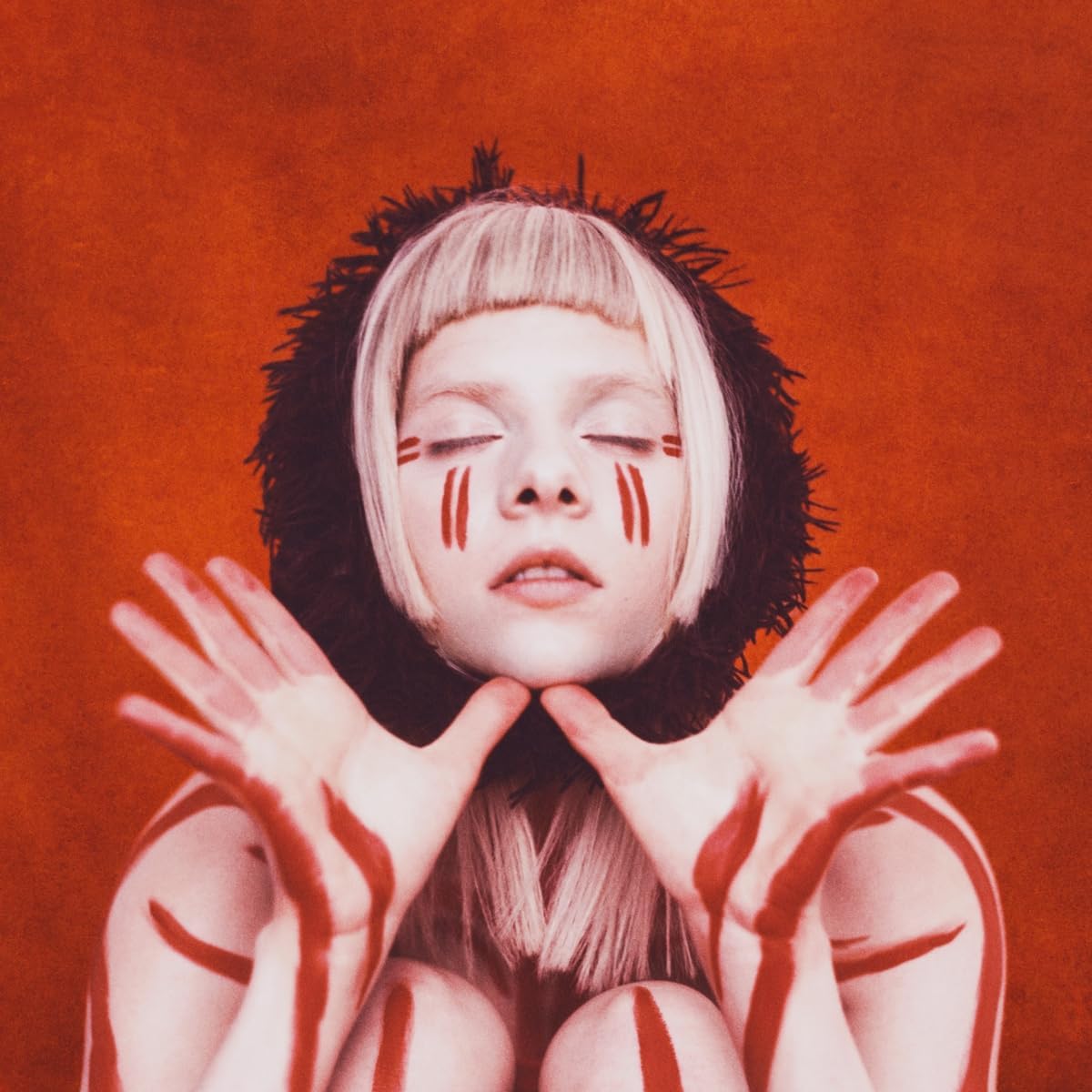 "A woman with blonde hair and red face paint against a red background."