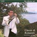 Man in white jacket playing a French horn outdoors, near water and trees.