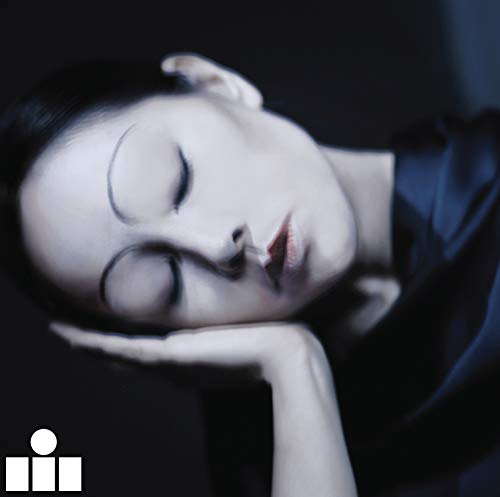 A woman with dark hair rests her head on her hand, eyes closed, against a dark background.