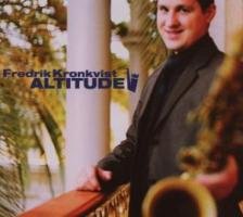 Man in a suit holding a saxophone on a balcony with trees in the background.