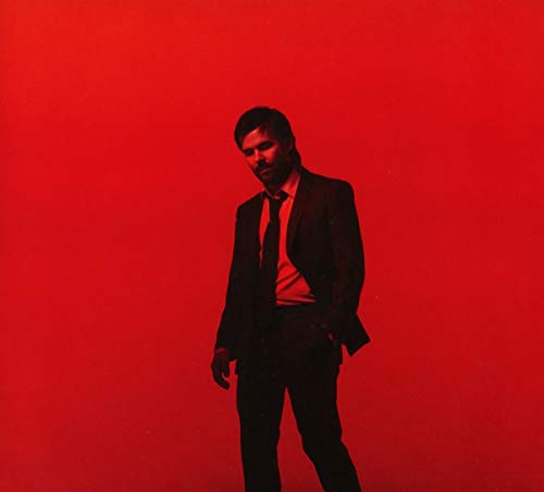 Man in a suit standing against a red background, looking down.
